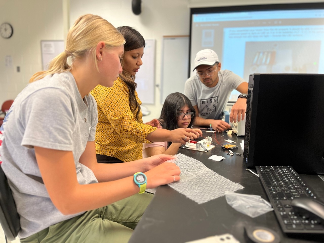 High school aged students watching intently as academy leader assists with an engineering project