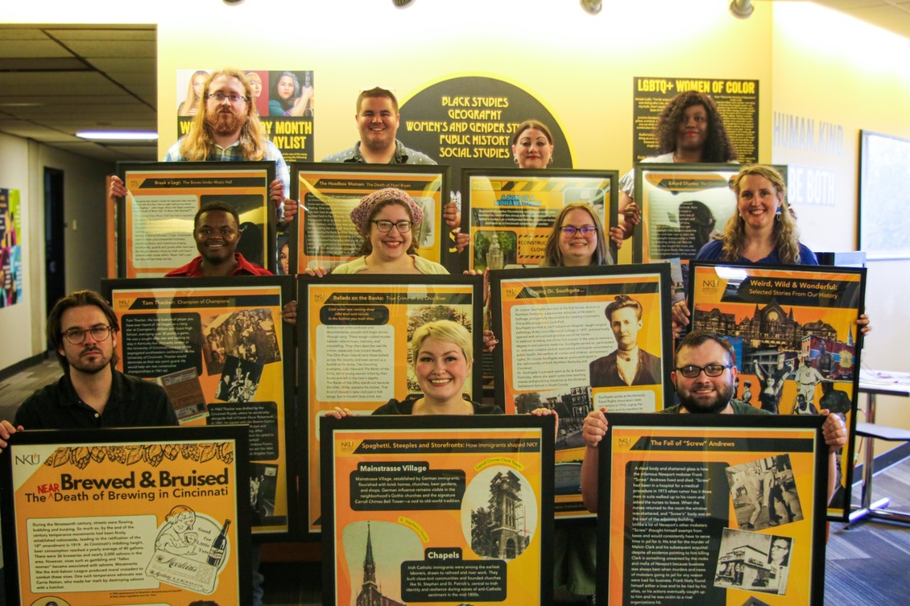 Students in NKU's Master of Public History program pose together with the posters they created for the Wild Weird and Wonderful exhibit.